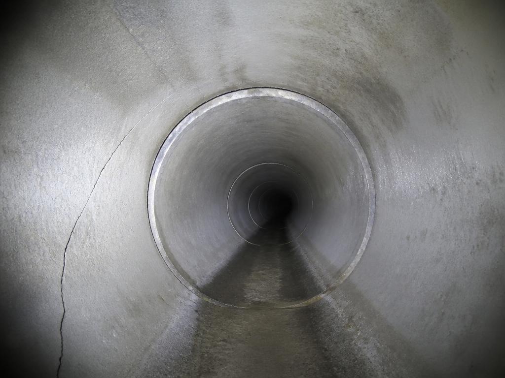 Inside a concrete drain pipe lit by an inspection camera, showing a crack and a joint